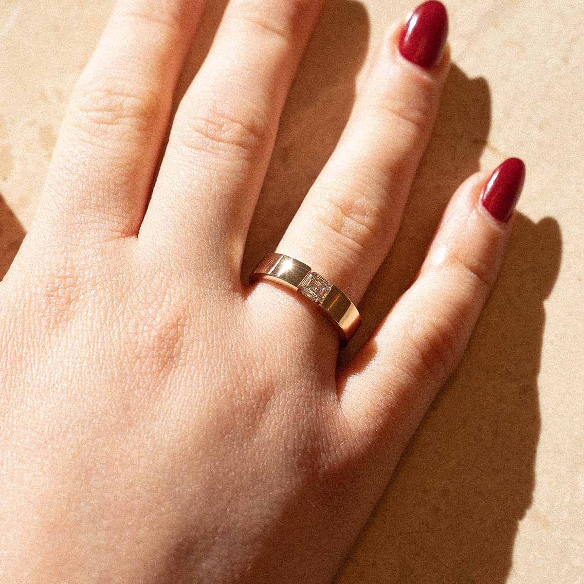 Model trägt matten Asscher-Verlobungsring in Gelbgold mit einem Lab-Diamanten