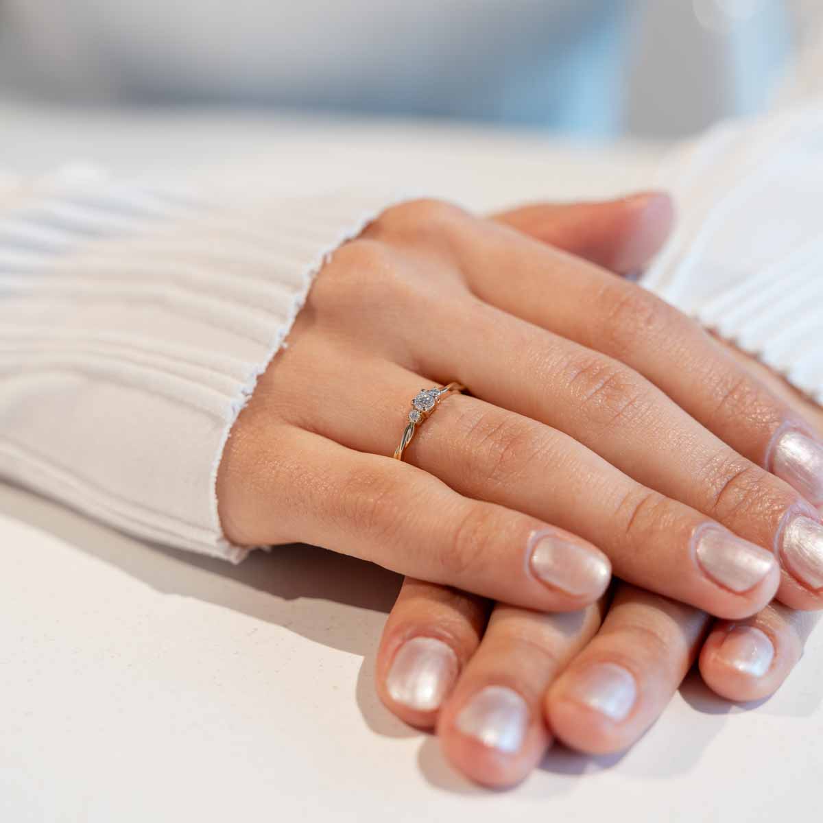 Hand mit gelbgoldenem Verlobungsring mit schlichtem gedrehten Ringband und Labor Diamanten