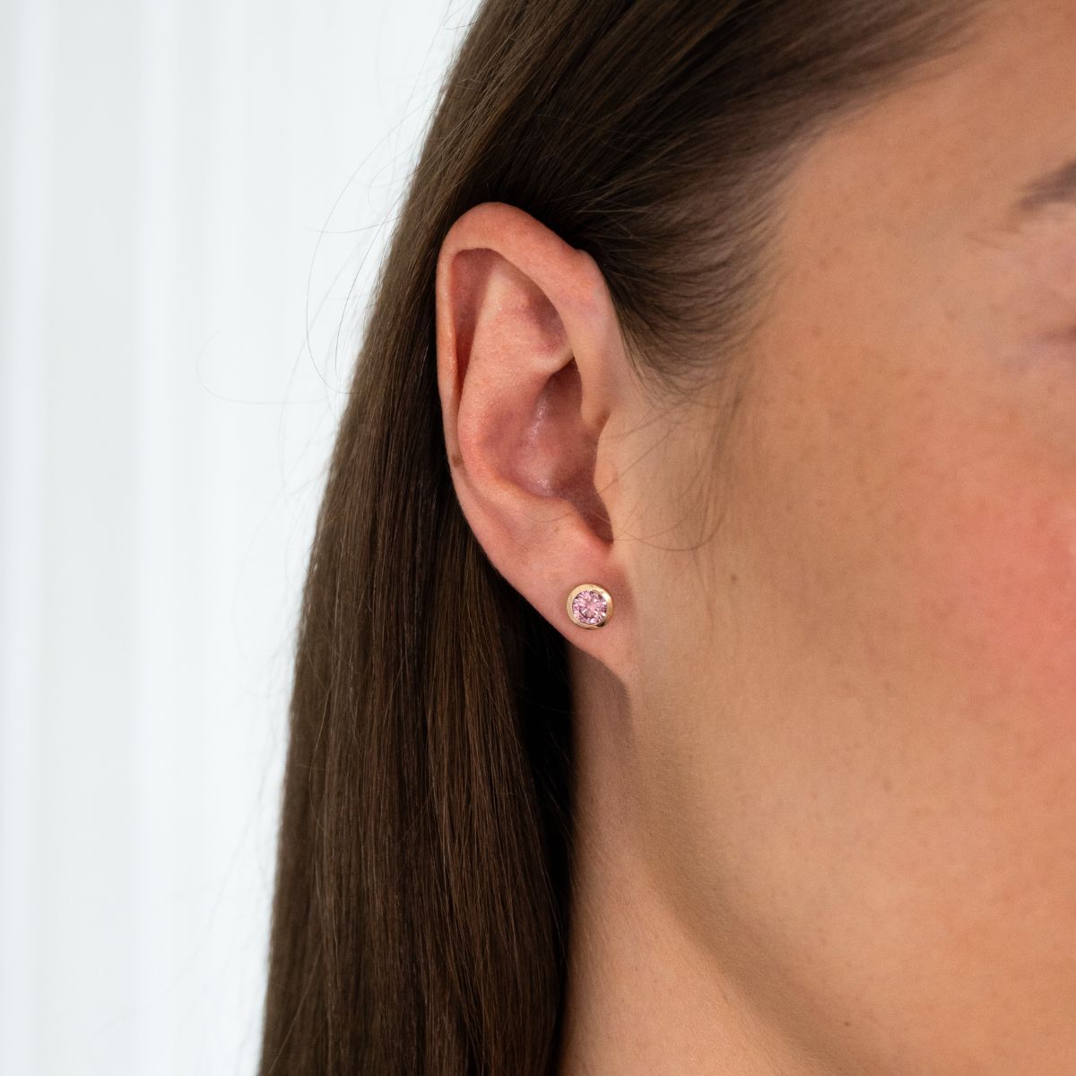 Nahaufnahme eines Ohrs mit einem kleinen, runden Ohrstecker mit rosa Diamant in Zargenfassung in 0.5ct.