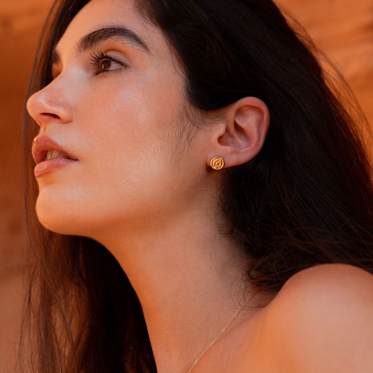 Model trägt goldenen Ohrstecker am Ohr und blickt in die Ferne
