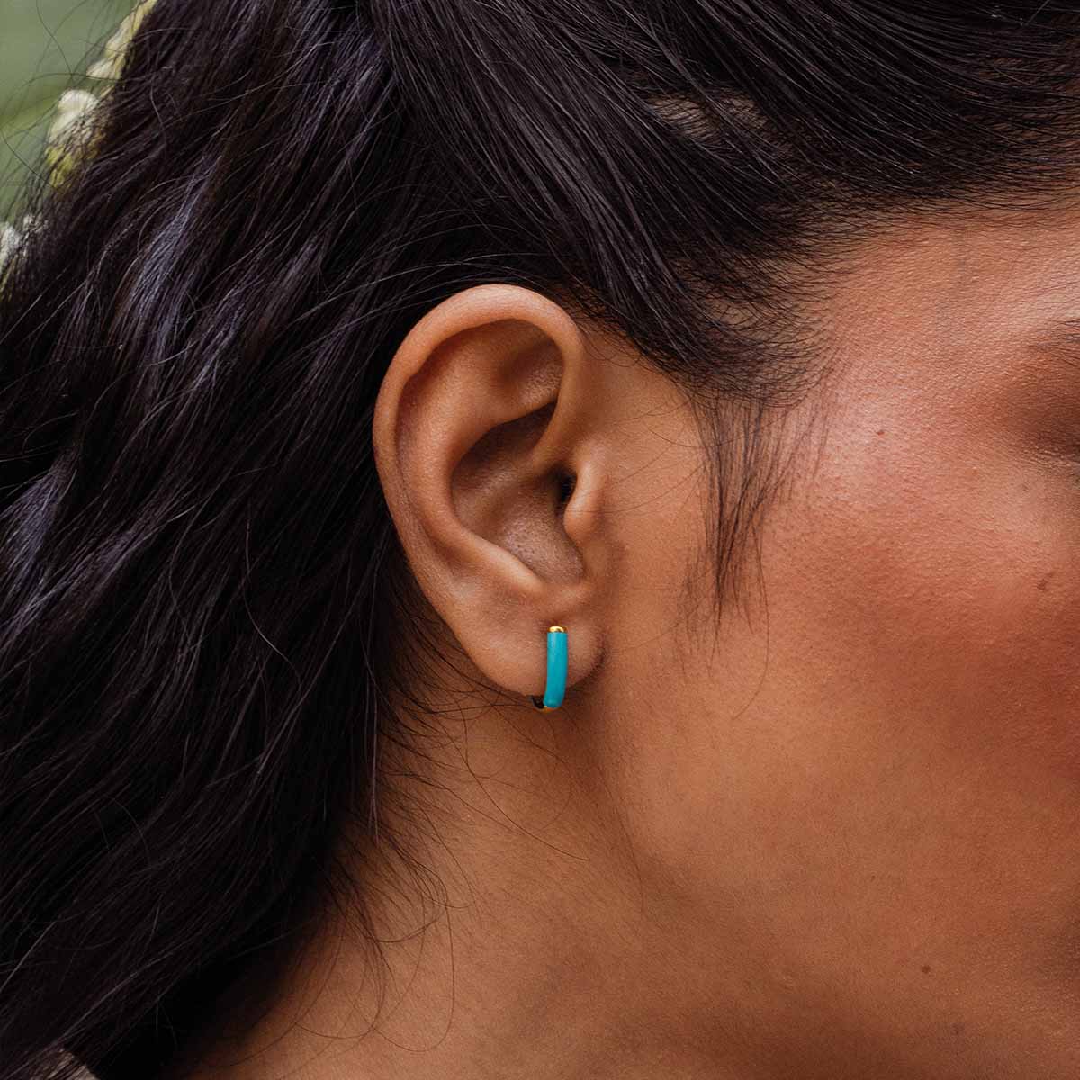 Model trägt U-förmige Kreolen mit goldener Fassung und Türkisem Detail in Nahansicht