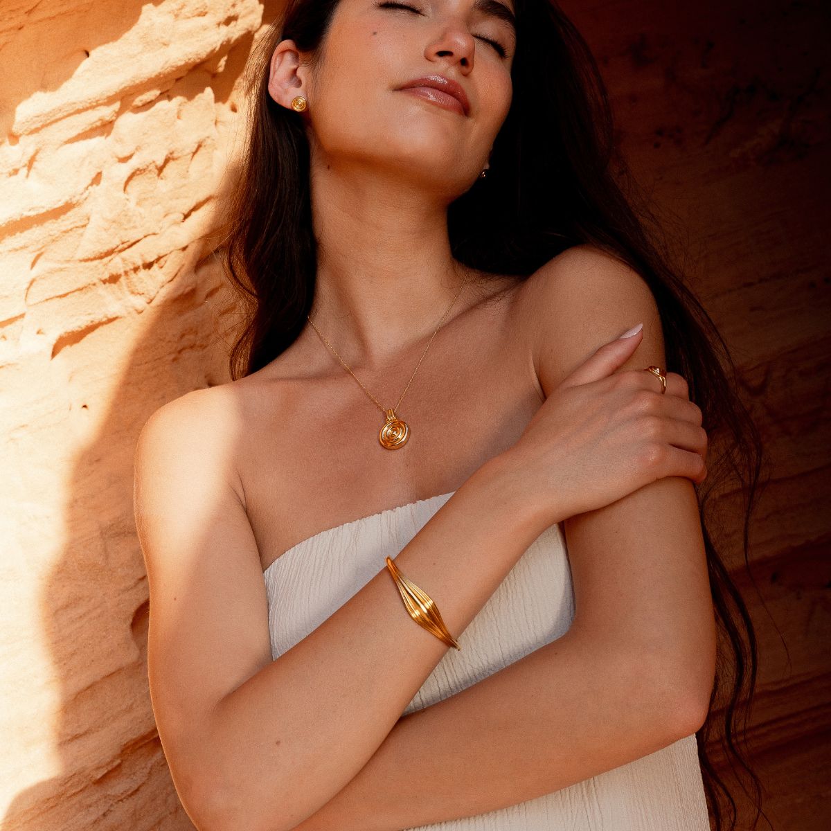 Model trägt goldenen Armreif und Kette mit verschränkten Armen