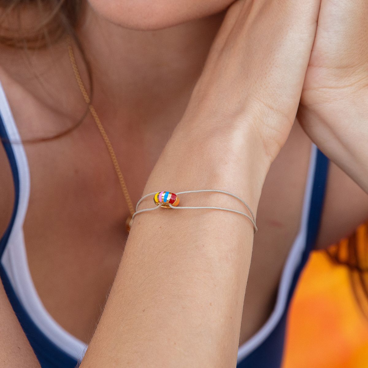 Model trägt Kordelarmband in beige mit runder Rondelle in gelbgold mit bunten Streifen.