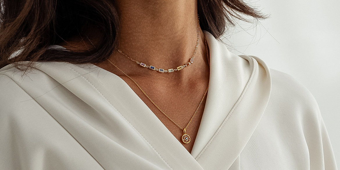 Zwei Goldketten mit bunten Edelsteinen an Frau in weißem Sweatshirt 