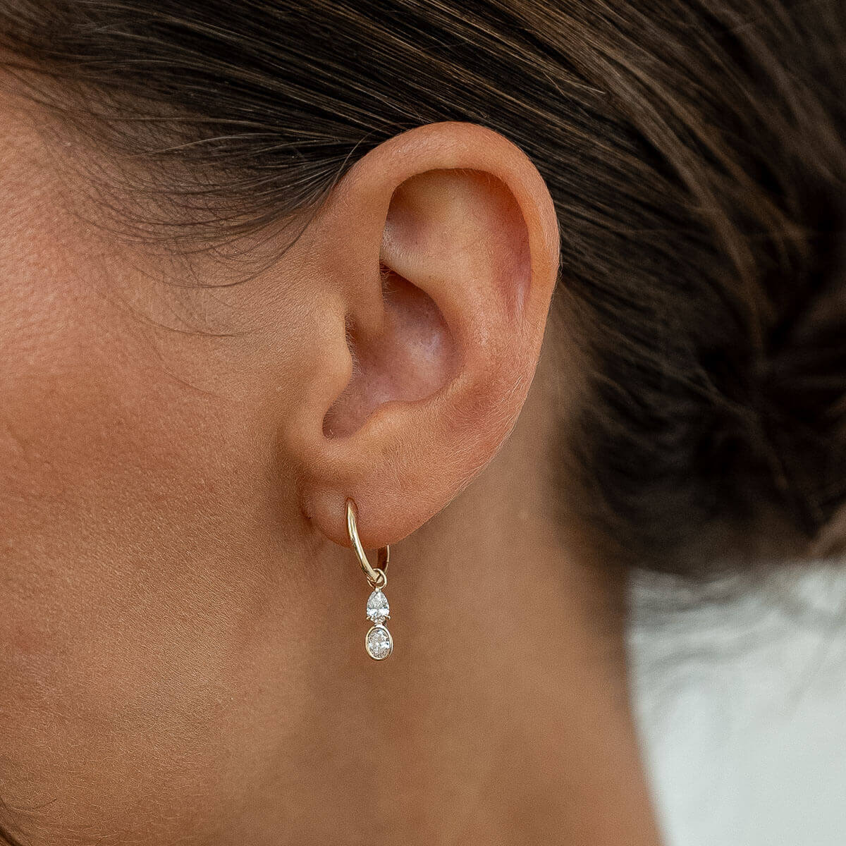 Model trägt Goldohrringe mit rund- und smaragtgeschliffenen Lab Diamanten