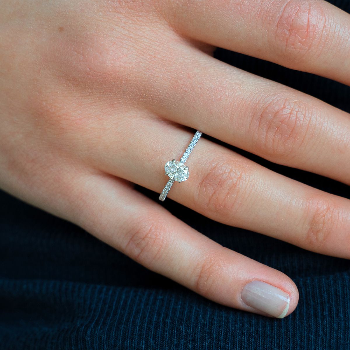 Model trägt Verlobungsring aus Weissgold mit ovalem Lab Diamant und Pavé-besetzter Ringschiene