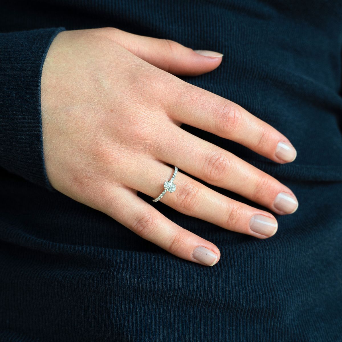 Model trägt Verlobungsring aus Weissgold mit ovalem Lab Diamant und Pavé-besetzter Ringschiene