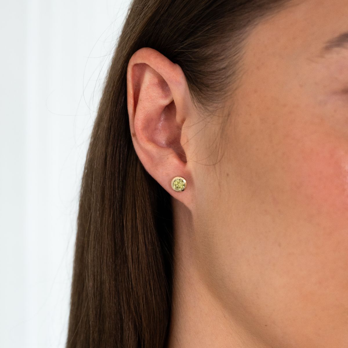 Nahaufnahme eines Ohrs mit einem kleinen, runden Ohrstecker mit gelbem 0.6ct Diamanten in Zargenfassung 