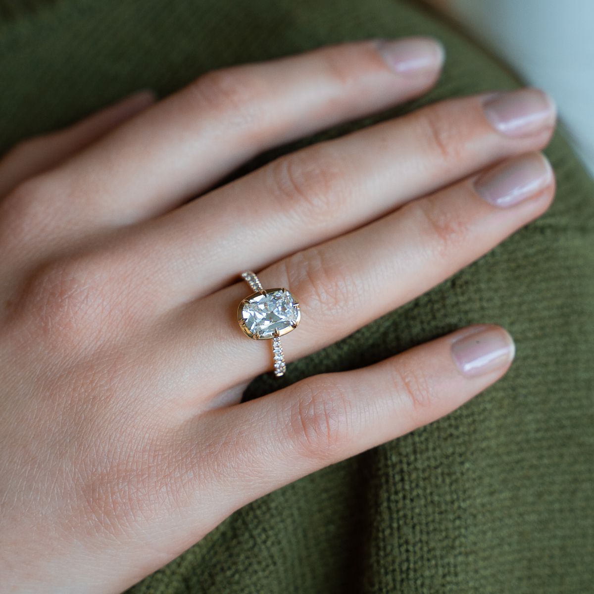 Model trägt Verlobungsring aus Gelbgold mit Lab Diamant im Kissenschliff und Pavé-besetzter Ringschiene