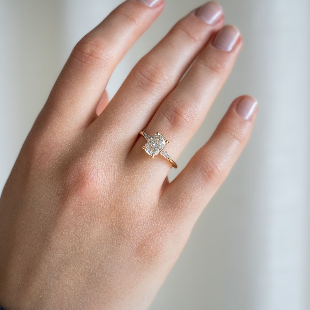 Model trägt Verlobungsring aus Gelbgold mit Lab Diamant im Elongated Cushion-Schliff und seitlichen Tapered Baguette Diamanten