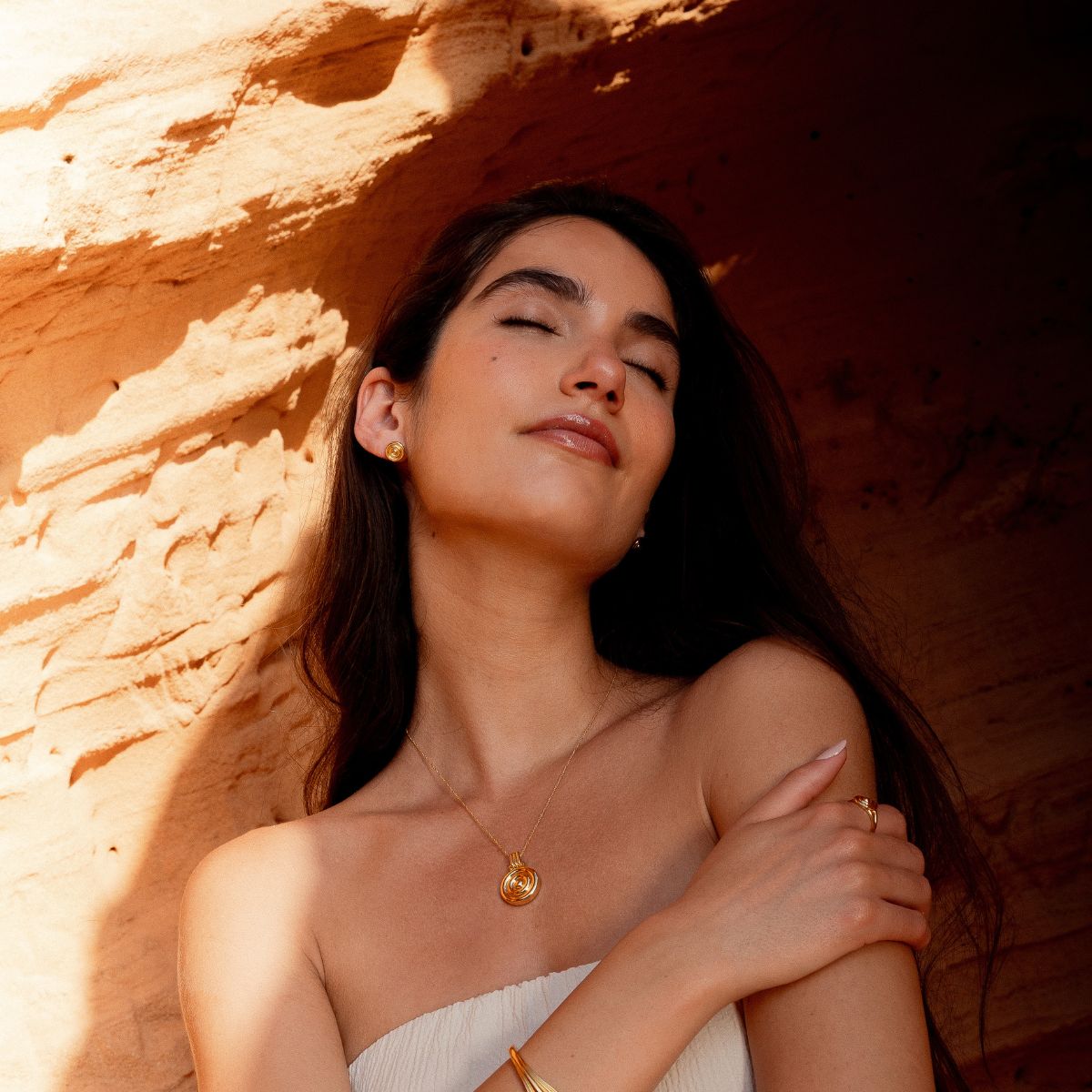 Model mit verschränkten Armen trägt goldene Ohrringe und weitere Schmuckstücke