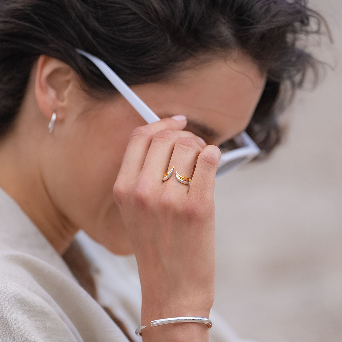 Das Model trägt einen Ring in Gelbgold & Weiß und fasst sich an die Brille.