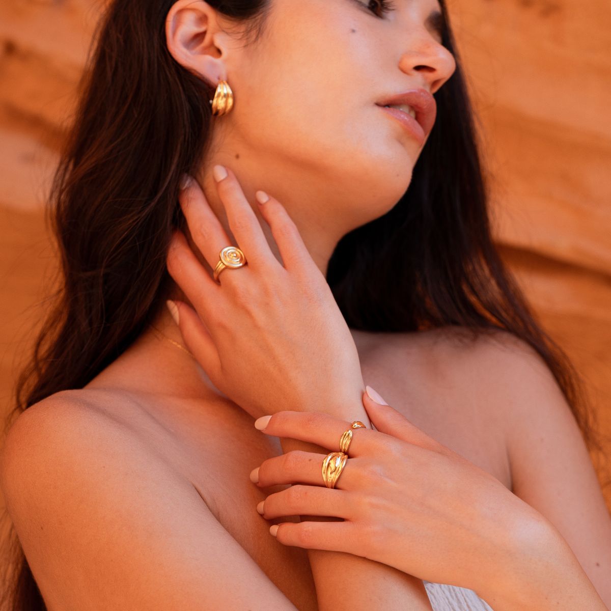 Model mit goldenen Kreolen, drei Statement-Ringen und hand am Hals