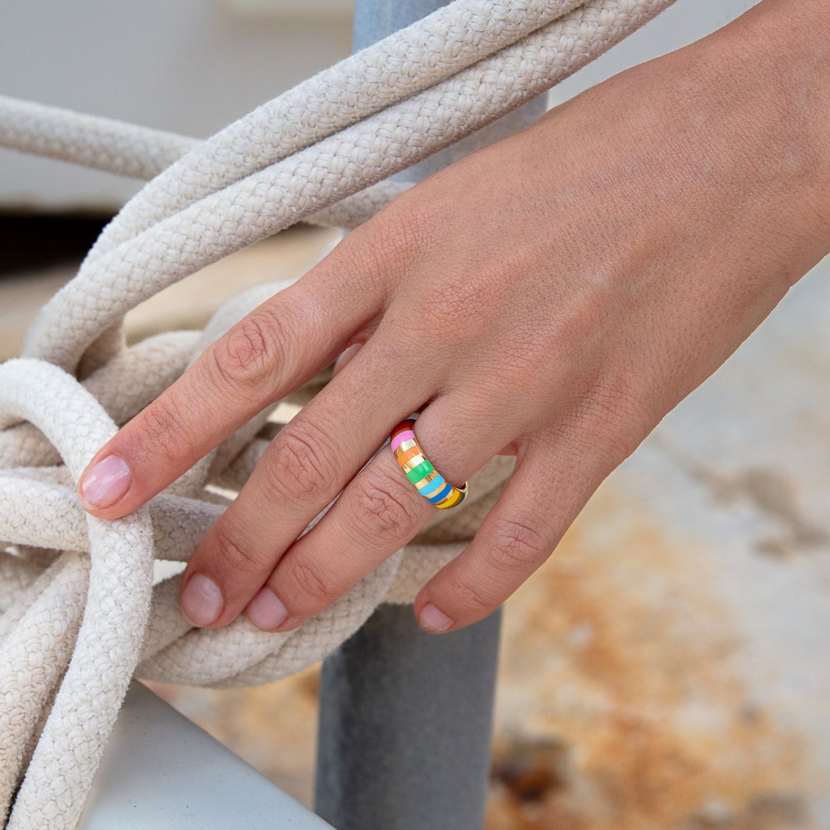 Model trägt einen Gelbgoldring mit bunten Keramikstreifen – Nahaufnahme am Finger.